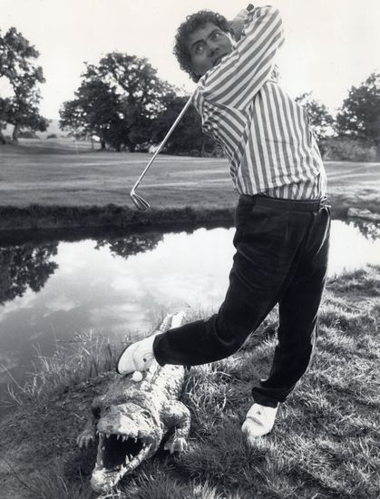Max Boyce swinging a golf club whilst standing on a fake crocodile